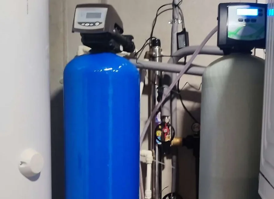 Dve kolóny s filtračnou náplňou a elektronickými riadiacimi hlavicami v technickej miestnosti rodinného domu vedľa zásobníka teplej vody